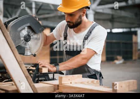 Side view, cutting the wood. Industrial worker in the warehouse. Stock Photo
