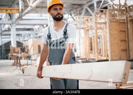 Front view, holding plank. Industrial worker in wooden warehouse. Stock Photo