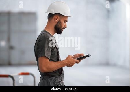 Side view, using digital tablet. Male worker is in the empty warehouse. Stock Photo