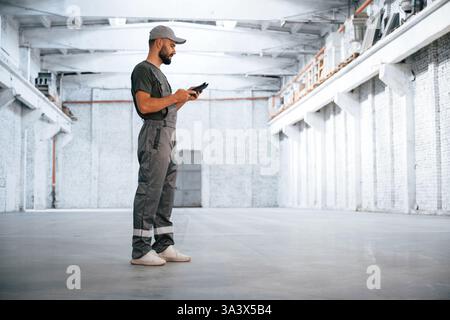 Black digital tablet in hands. Male worker is in the empty warehouse. Stock Photo