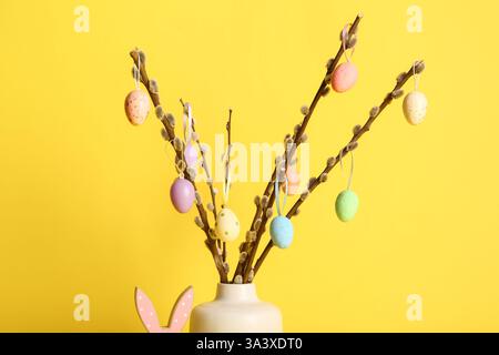 Vase with willow branches and colorful Easter eggs on yellow background Stock Photo