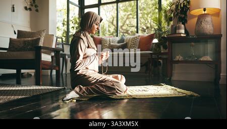 Muslim woman, prayer beads and home for worship, Islam or start morning with religion for Allah in living room. Person, hijab and Ramadan on floor to Stock Photo