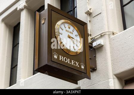 Rolex logo sign and gold brown classic clock hang on the wall at a shop in a shopping street. Rolex SA is a British-founded Swiss watch designer. Stock Photo
