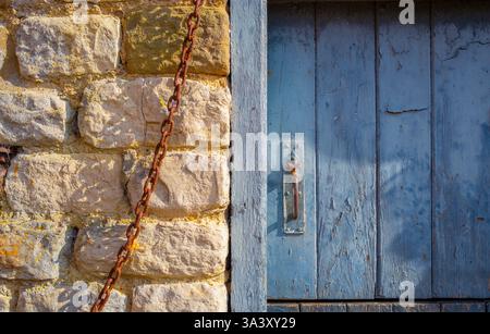 Rusty metal chain and rough stone wall and light blue wooden barn door, peeling paint and metal latch. Stock Photo