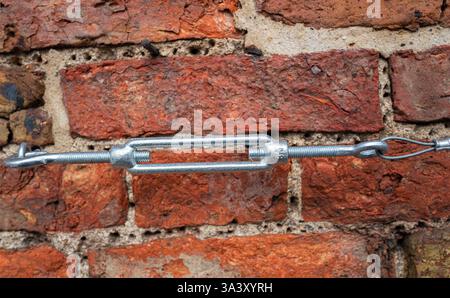 Standard galvanised steel Turnbuckle with hook and shackle attached to a brick wall with wire attached. Stock Photo