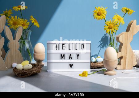 HELLO MAY text on Lightbox with bunny wooden figures eggs and fresh flowers. Easter composition content still life. Christian symbols of spring holiday  Stock Photo