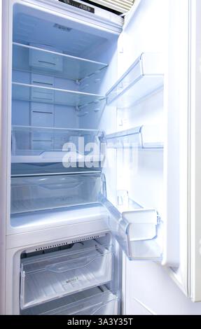 A refrigerator is open and the inside is empty. The door is white and the shelves are clear Stock Photo