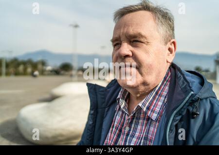 Senior man portrait in casual outdoor clothing, looking into distance with thoughtful expression. Symbol of aging, retirement, wisdom, and peaceful outdoor lifestyle. Stock Photo
