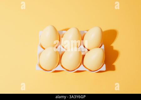 Minimalist yellow eggs in a white tray on a monochrome yellow background, creating a simple and modern composition with light and shadows. Easter Stock Photo