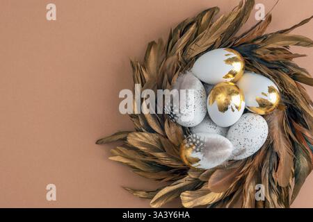 Luxury Easter wreath with white eggs decorated with bronze feathers on a brown background. Top view, flat lay, copy space. Stock Photo