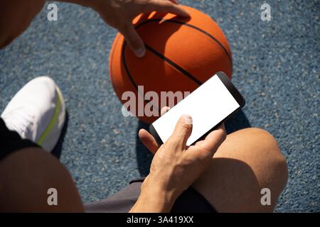 Basketball player using smartphone and texting social media during game interval, Outdoor training. Top view. Close up. Stock Photo