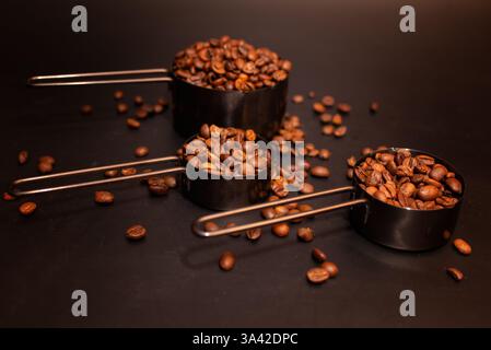 coffee beans roasted in measuring cups on a dark background scattered on the table Stock Photo