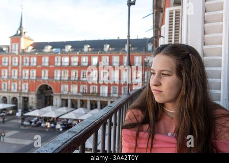 A young woman sits on a balcony, admiring a beautiful cityscape Stock Photo