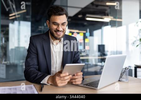 Successful businessman using tablet computer inside office at workplace. Man smiling happily, reading online financial report. Stock Photo