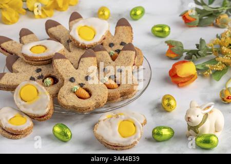 Bunny biscuits and egg biscuits decorated with icing next to Easter eggs and spring flowers Stock Photo
