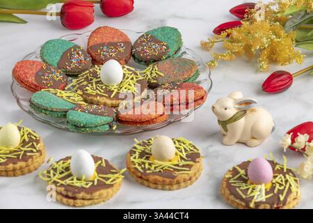 Plate with colourful Easter biscuits, decorated with eggs, next to red tulips Stock Photo