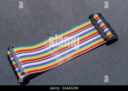 A rainbow-colored ribbon cable with connectors lying on a dark surface Stock Photo