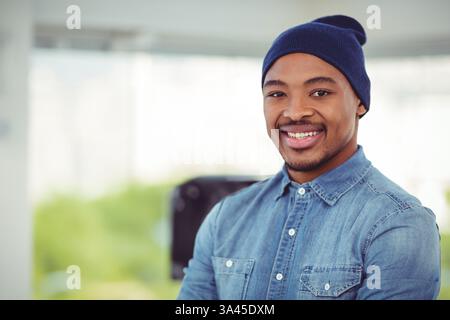 Smiling man in denim shirt and beanie standing confidently in office, copy space Stock Photo