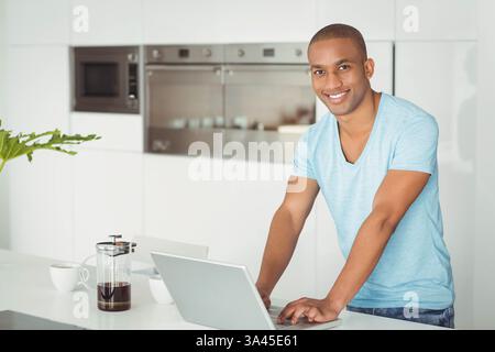 Smiling African American man using laptop in modern kitchen, enjoying morning coffee Stock Photo