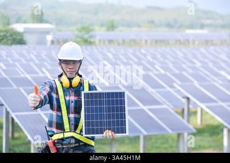 Engineer holding a solar panel standing in front of rows of solar panels at a solar powered station, Thailand Stock Photo