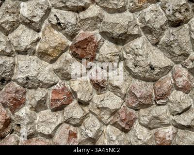 Natural beige cobble stone wall with slight red color and grunge texture. Rough cut cobbles and gravel for outdoor  wall finishes. Seamless background Stock Photo
