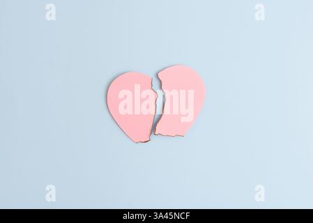 Broken heart concept made with burnt pink paper heart on pastel blue background. Minimal creative love idea. Valentines Day concept, top view Stock Photo