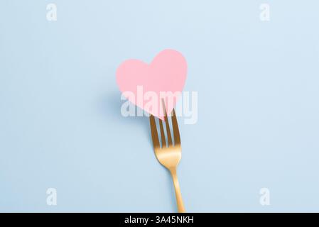 Top view of golden fork with pink paper heart on pastel blue background. Minimal Valentine's Day dinner invitation card, top view, copy space Stock Photo