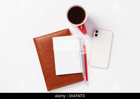 Brown notebook, red pencil, white smartphone and red cup with coffee on white background. Morning plans for the day, workspace Stock Photo