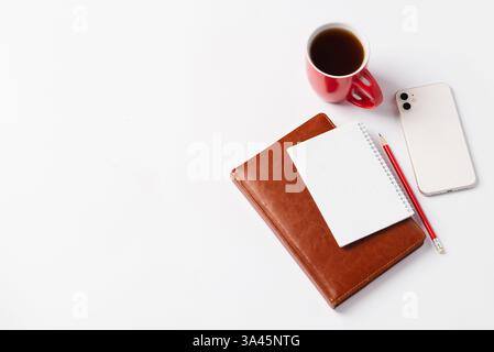 Brown notebook, red pencil, white smartphone and red cup with coffee on white background. Morning plans for the day, workspace Stock Photo