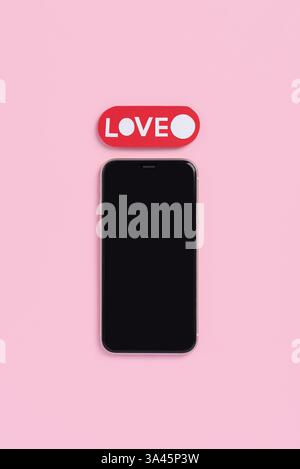 Top view of mobile phone with blank screen and word love on pastel pink background. Mockup template for Valentines Day. Love and technology concept Stock Photo