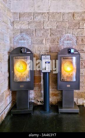 Barcelona, Spain 21. July 2024, Two souvenir medal vending machines with a change machine in the middle, standing against a stone wall in Barcelona Stock Photo