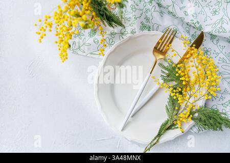 Elegant spring table decor with golden cutlery and mimosa flowers Stock Photo