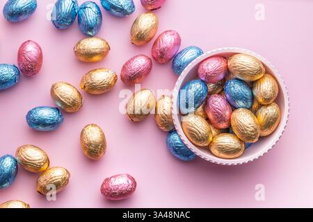 Chocolate easter eggs wrapped in multi colored foil in bowl on a pink background. Top view. Stock Photo