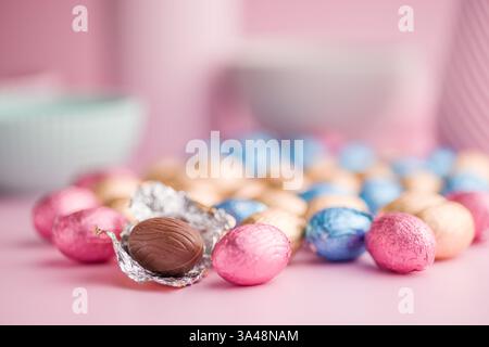 Chocolate easter eggs wrapped in multi colored foil on a pink background. Stock Photo