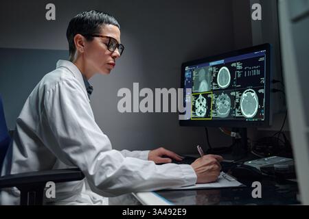 Professional wearing glasses analyzing medical data on monitors in modern lab setting indicating focus and expertise in medical research without natural light Stock Photo