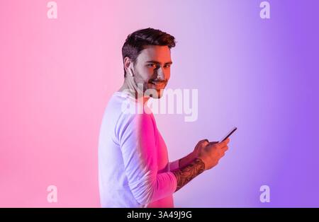 Young man smiling while using smartphone against colorful backdrop Stock Photo