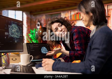 Startup intern asks questions to senior technician coding advanced AI algorithm and machine learning models enhancing automation. Employee requests help from CTO manager in Silicon Valley workplace Stock Photo