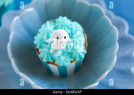 Easter cupcake with white rabbit in a blue dessert plate.Blue Cupcakes with Easter Topping.assortment of holiday baked goods.Cute Bunny Decorated Stock Photo