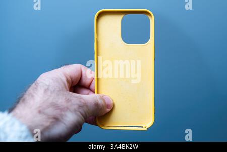 Paris, France - Mar 10, 2025: A hand holds a damaged yellow plastic iPhone case viewed from a frontal point of view, showing the broken lower edge and Stock Photo