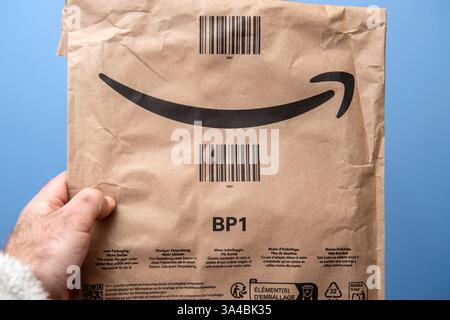 Paris, France - Mar 10, 2025: A male hand holds a crumpled brown Amazon Prime paper envelope featuring the signature black smile logo, barcodes, and m Stock Photo