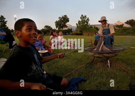 Aug. 9, 2014 - Chicago, IL, USA - Wyatt Gilmore, 7, left, roasts a marshmallow for his very first s'more as storyteller John Elliott tells stories around the campfire. Campers spent the night Aug. 9, 2014 on the back lawn of the Garfield Park Conservatory on Chicago's west side. They fished, ate hot dogs and marshmallows over the open fire and slept in tents. (Credit Image: © Nancy Stone/MCT/ZUMA Wire) Stock Photo