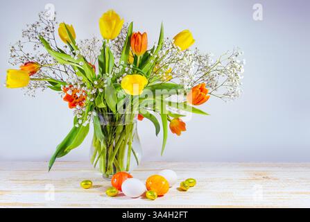 Bouquet of yellow and orange tulip and some Easter eggs on a light painted wooden table, spring decoration and holiday greeting card, gray background, Stock Photo