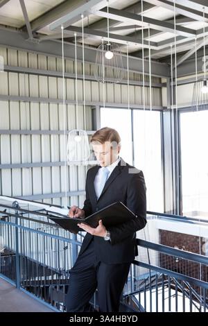 Businessman in suit reviewing documents in modern office building hallway Stock Photo
