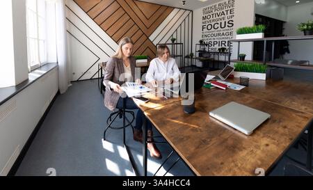 Two professionals collaborate in a modern office, analyzing data and discussing strategies during a productive work session Stock Photo