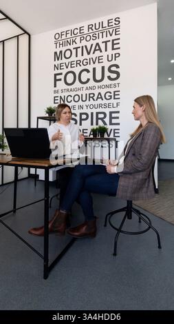 Engaging discussion between two women in a modern office setting focused on motivation and self-improvement strategies Stock Photo