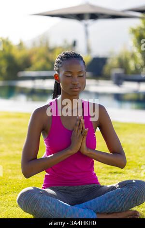 Young woman meditating by pool, practicing yoga with serene expression outdoors, copy space Stock Photo