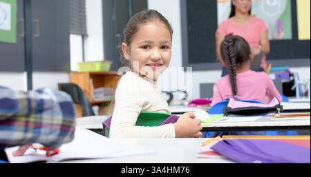 In school, girl smiling and holding book in classroom, sitting at desk Stock Photo