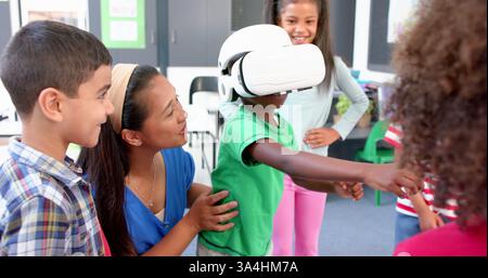 In school, children using VR headset with teacher guiding them in classroom Stock Photo