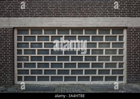 A symmetrical glass brick wall with a modern, geometric pattern framed by dark brown bricks and concrete elements. Stock Photo