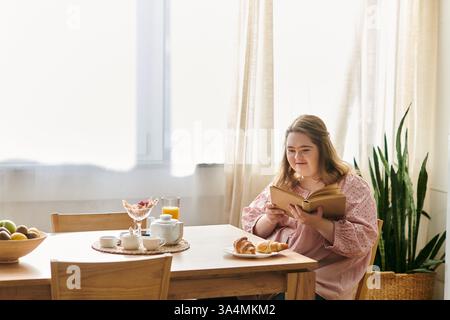 A young woman with Down syndrome enjoys reading and sweet treats in her cozy home. Stock Photo
